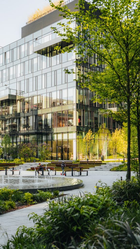 Spacious urban park surrounded by modern glass architecture with benches and fountain.