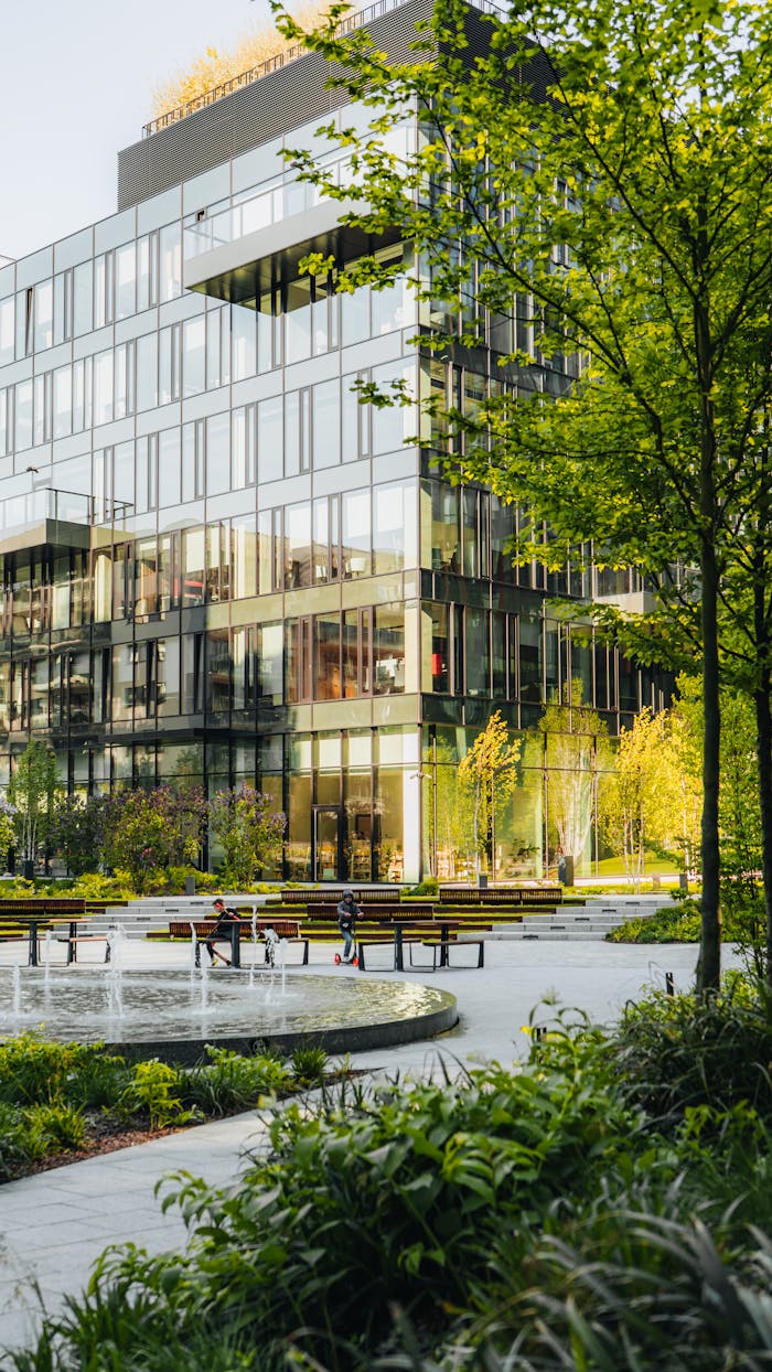Spacious urban park surrounded by modern glass architecture with benches and fountain.